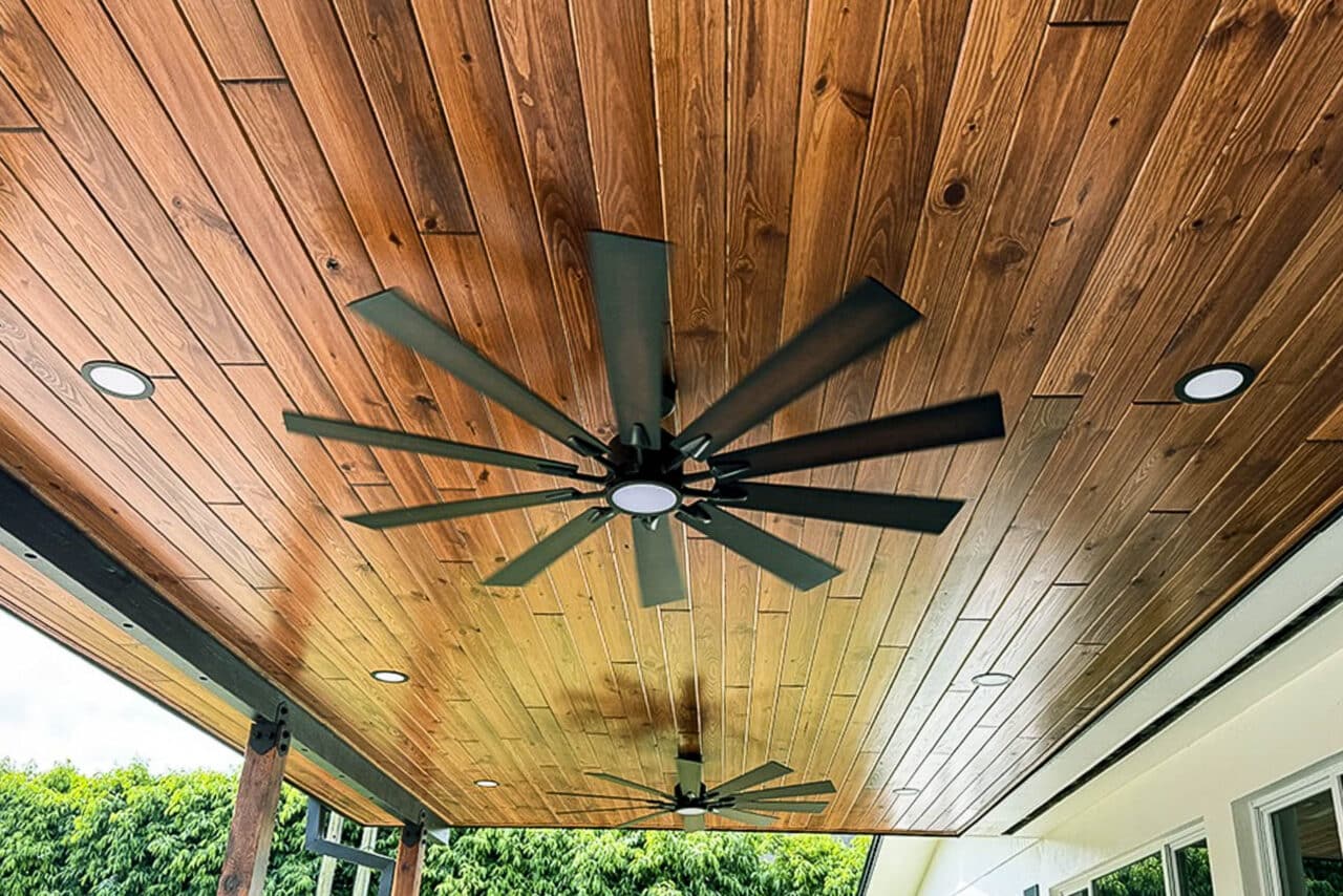 Wood plank ceiling with recessed lighting and ceiling fans installed on a covered outdoor deck