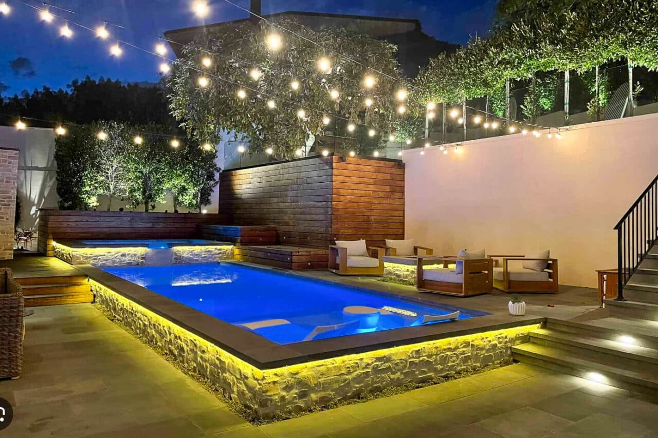 Outdoor deck and pool area with string lights and integrated deck lighting at night